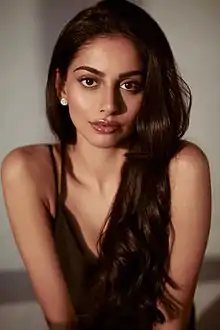 close-up of Banita Sandhu wearing a black sleeveless blouse, staring directly at camera