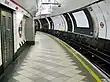 The interior of a building with a rounded roof and walls, a grey door on the left, a railway track on the right, and a man walking in the middle