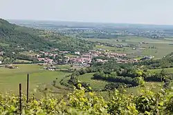 A hilly landscape with a small town with white buildings, red roofs, and a belltower.