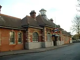 A red-bricked building with a sloping, black roof, four chimneys, and a sign that reads "UNDERGROUND" under a blue sky with white clouds