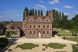 Red brick house with a single storey section to the left, and trees to the right