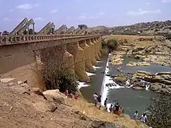 several commune members near a river with a bridge nearby