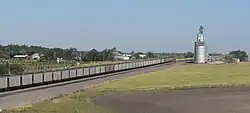 Cluster of houses seen over railroad tracks occupied by train; metal grain elevator