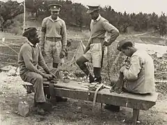 Two (standing) Bermuda Militia Infantry soldiers wearing the 1905 style khaki peaked cap, and two (seated) wearing the new khaki side cap, circa 1940