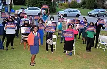 Bernice Mireku-North stands in front of several campaign signs and supporters at a campaign rally