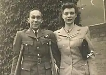 black and white photograph of a black man using crutches standing next to a white woman. Both people are wearing uniforms