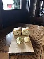 two tall biscuits and two balls of piped butter on a wooden serving board