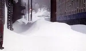 Ground-level view of deep snow and drifts between two city buildings.