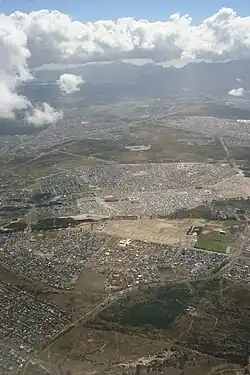 An aerial photograph of Blue Downs in the foreground and Mfuleni laying just beyond. Picture is taken of these two areas stretching to the west towards Table Mountain. Ikweze Park (on the left) and Delft (to the right) lay beyond.