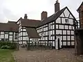 The 19th-century farm building, painted in mock-Tudor style. This later building dominates the site from the farmyard and strikes the visitor first.