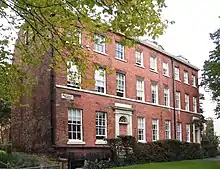 Colour photograph of Botany House consisting of a terrace of three houses. The houses are constructed of red brick with stone details and a slate roof. The whole house has three storeys and nine first-floor windows, with doorways below windows three and nine.