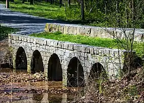 Stone bridge with five circular openings allowing a leaf-littered creek to pass through slowly