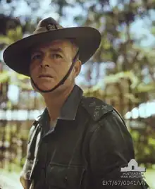 Head and shoulders photograph of a middle-aged caucasian man wearing a green uniform and slouch hat, standing side on to the camera and looking past it.