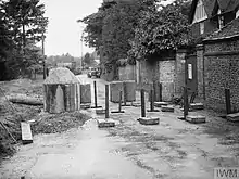 A series of concrete blocks and upright steel girders, block the road from use by vehicles.