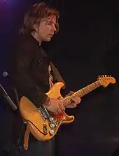 Lukas Nelson playing guitar in a black T-shirt and bandana.