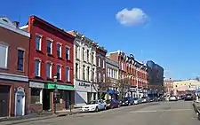 A row of three-story brick commercial buildings in different colors, seen from across a street at an oblique angle. Near the rear one has scaffolding covered by black mesh.