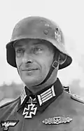 Black-and-white portrait of a man wearing a steel helmet, military uniform with an Iron Cross displayed at his neck.