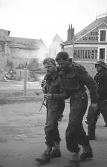 two British soldiers one appears wounded being helped by his comrade with a German guard in the background