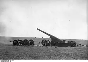 A large gun on its firing plate pointing to left in open ground. A wheeled carriage is nearby.