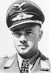 A man wearing a peaked cap and military uniform with an Iron Cross displayed at the front of his uniform collar.