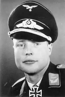 A man wearing a military uniform, peaked cap, and an Iron Cross displayed at the front of his uniform collar.