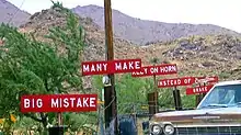 A set of 6 white-on-red signs with white block text along the side of a road, reading in order "BIG MISTAKE", "MANY MAKE", "RELY ON HORN", "INSTEAD OF BRAKE", and, stylized, "Burma-Shave".