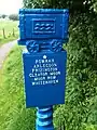 C2C Milepost showing Rowrah, Arlecdon, Frizington, Cleator Moor, Moor Row and Whitehaven. At the top of the post is a depiction of a quarry rail cart used to move iron-ore and limestone.