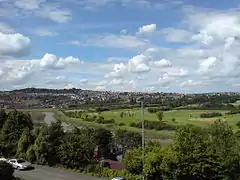 A photograph taken from a house window on Caerleon Road in St Julians. The view crosses the river Usk and in the distance is the Caerleon Golf Club, and behind it, the settlement of Caerleon, on the hill with rows of houses visible. At the far right are the visible buildings of Caerleon Comprehensive School and its sports facilities.