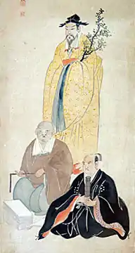 One man standing behind two seated men; they all are in particularly formal garb