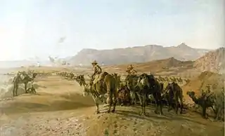 A large number of men mounted on camels in a treeless desert. There is a town in the distance, and bare rocky mountains beyond.