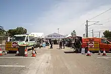 A crowd of people in the station's carpark. There are gazebos set up and a coffee van and ambulance parked.