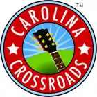 The Carolina Crossroads logo is circular with two concentric rings. The outer ring is red with the white text "Carolina" arcing around the top of the circle, "Crossroads" around the bottom, and five-pointed stars at the left and right of the ring. The inner circle has green in the bottom and blue in the top; the green appears to be a hill. The neck and headstock of a guitar rise from the bottom right edge; the headstock of the guitar is placed on the horizon formed between the green and blue sections. White streaks, evocative of sunbeams, radiate from the headstock.