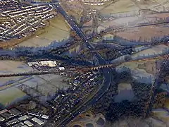 The M80 above the arches turns to point approximately north up the hill towards Stirling. The railway cuts across the picture left to right. The canal, shown by a line of trees, crosses the picture above it with the white roofs of the CMS buildings at between them at the site of the old railway station. The Red Burn (SUDS) ponds can be seen at the bottom of the picture. Cumbernauld's Wardpark East can be seen at the bottom left hand corner. The bridge north of the viaduct leads to Allandale and bridges further north separate Banknock at the top left from Haggs.