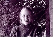 Purple-tinted photograph of a smiling, middle-aged white woman in front of a forest background.