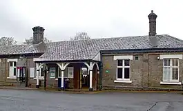 A brown-bricked building with two brown-bricked chimneys, some trees in the background, and a speed bump in the foreground all under a blue sky