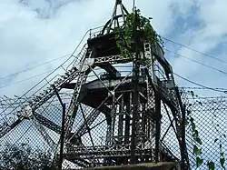 Metal superstructure of a mine shaft, seen through a fence at ground level