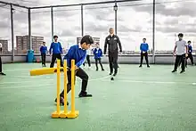 A boy striking a cricket ball on the rooftop of a school