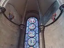  A semi-circular area with stone walls, a domed ceiling and a tall stained glass window with prominent circular decorations.