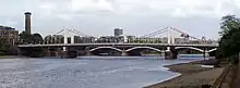 Side view of suspension bridge over a wide river. Two sets of towers, each about a quarter of the way from the river's edge, hold up the bridge.