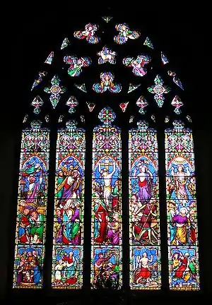 This stained glass window is divided into five long sections, above which the stone tracery looks like a lacey medallion. The colours are not like Medieval glass; there is a lot of bright red, pale blue, apple green, mauve and pink.