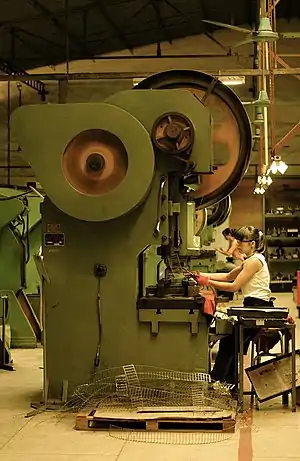 Seated female workers making knives on machinery with large spinning drums