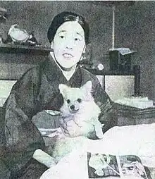 Black and white photograph of a seated woman wearing a kimono. She is holding a small white dog.