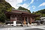 Wooden building with a raised floor, a hip-and-gable roof and an enclosing open railed veranda.