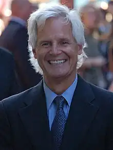 A man with white hair is looking and smiling at the camera.