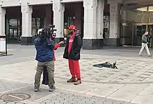 Two reporters, one with a camera, interview Amazon Labor Union President Chris Smalls outside of the NLRB office.