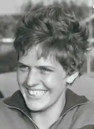 A smiling young woman with short hair, tousled by wind outdoors