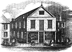 A black-and-white engraving depicting a street scene with a 2.5-story church with mullioned windows at center.