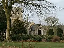 Stone building with square tower, partially obscured by trees.