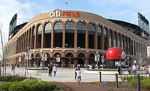 The exterior of a baseball stadium, which has a round brown entrance area with a white and orange "citiFIELD" on top.