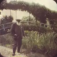 A grainy photo of a bearded man standing before a bridge